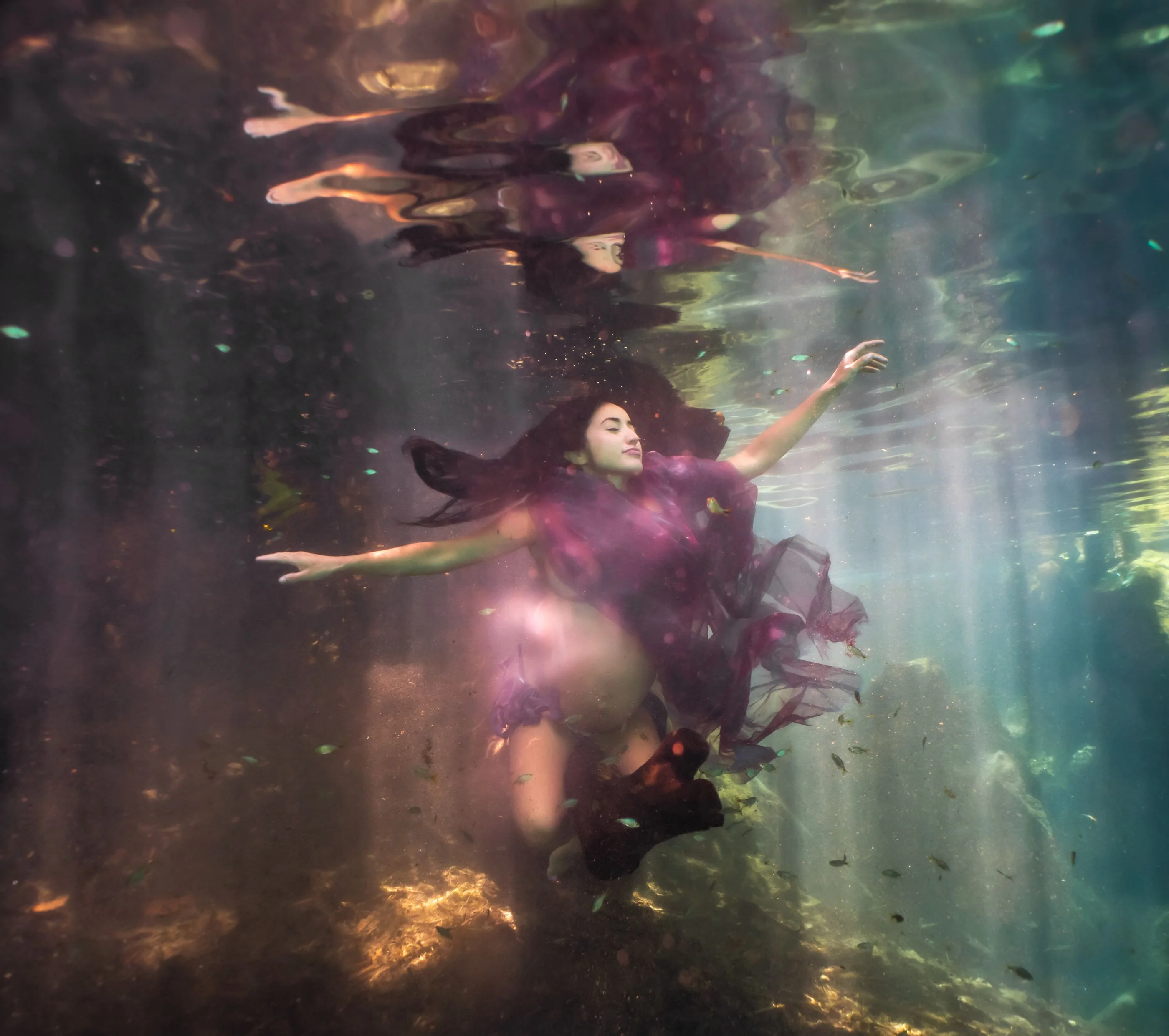 Two swimmers in a shaft of light in the cenote